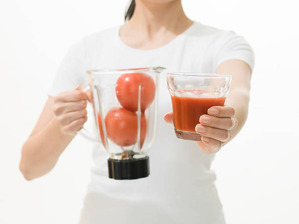 woman holding glass of tomato juice and juicer