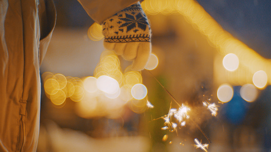 Woman in gloves and winter coat holding sparkler during illuminated Christmas night
