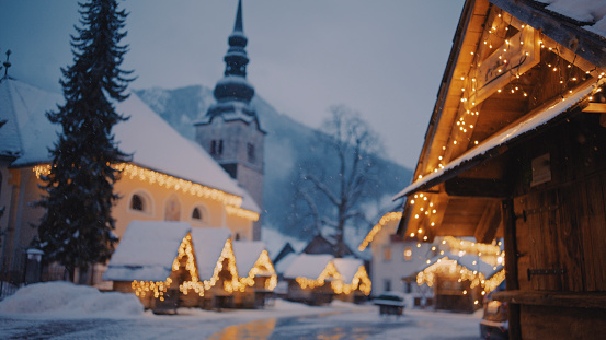 Illuminated decorated christmas market and Church of the Assumption of Virgin Mary at snowy alpine village Kranjska gora in winter