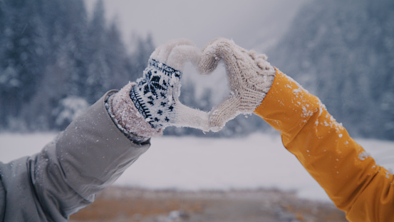 Two women friends in warm clothing making heart sign gesture with hands on a cold winter day