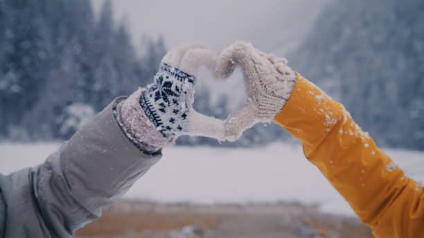 Two women making heart sign gesture in knitted woolen winter gloves on cold winter day stock photo