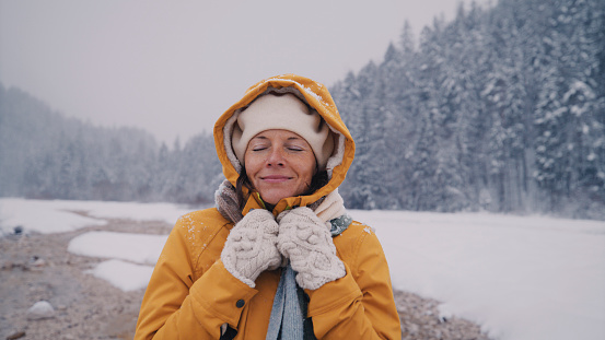 Carefree woman in warm clothing having fun in snow with her eyes closed