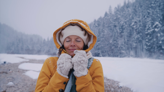 Carefree woman in warm clothing having fun in snow with her eyes closed