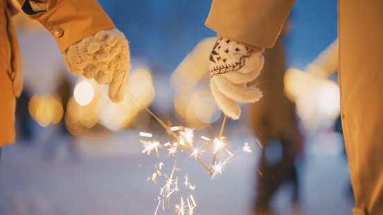 Hands of two women friends in warm clothing holding sparklers during Christmas celebration at Kranjska Gora town
