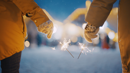 Hands of two women friends in warm clothing holding sparklers during Christmas celebration at Kranjska Gora town