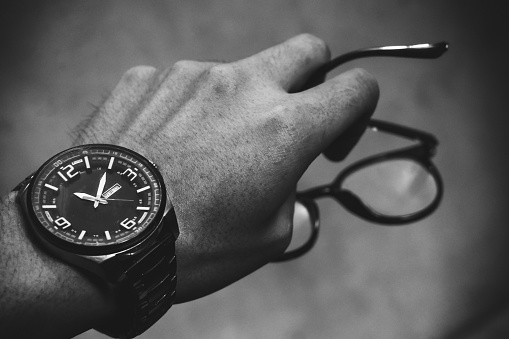Man's hand wearing a watch and holding glasses