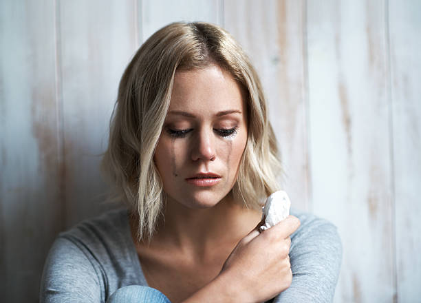 Feeling alone and lonely A pretty young blonde woman looking down while she is crying wiping tears stock pictures, royalty-free photos & images