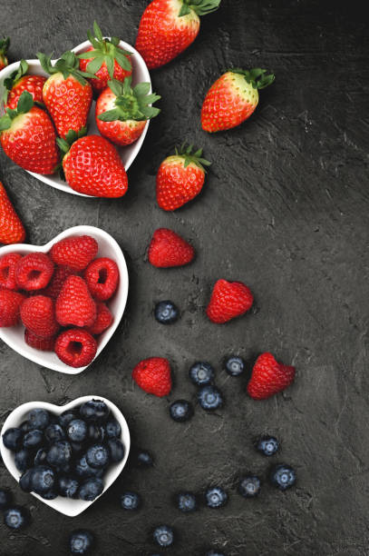 raw berries in a ceramic heart-shaped bowls on a black table.