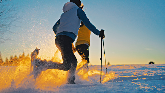 Silhouette of two women skiers snowshoeing or running on snowy slope during dawn splashing powder snow
