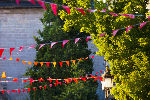Street feast decorations, rows of  red bunting at dusk, oak trees,  stone building exterior facade, old-fashioned  street light. Lugo city, Galicia, Spain.