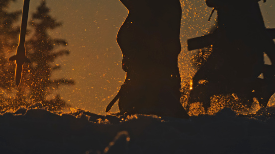 Silhouette low section of skier with ski equipment on snowy winter slope during sunset