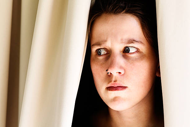 istock Worried young brunette looks sideways through drapes frowning nervously 174813157
