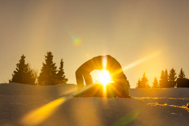 Woman practicing bridge pose on snowy hill with her pet dog during sunset
