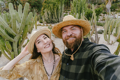 A portrait of smiling couple in a Western-style desert landscape with cacti. Selfie together during vacation in Latin America. Travel and honeymoon concept.