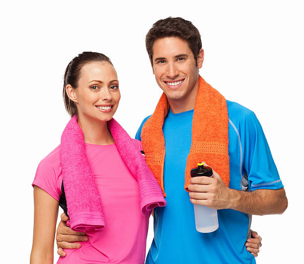 Portrait of young couple standing together with towels around their necks after a gym workout. Horizontal shot. Isolated on white.