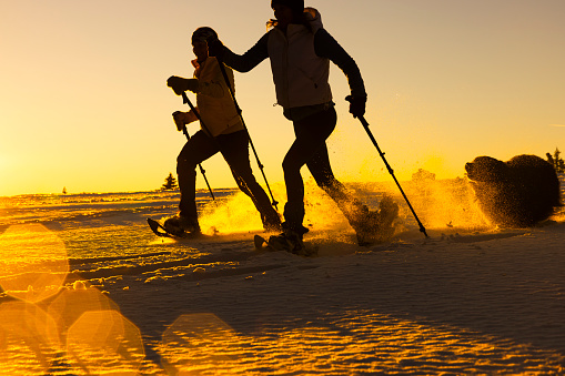 Silhouette of two women in warm clothing skiing on snowy slope during sunset