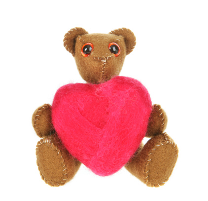 A small felt teddy bear holding a felted heart. (both made by me). Isolated on white.