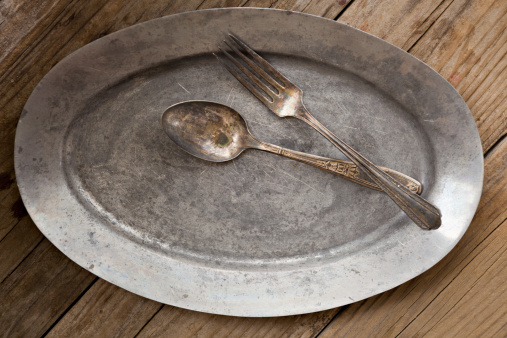 An overhead close up shot of an old pewter platter and some tarnished silverware. Shot on a grungy old wooden table.