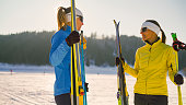Two women in warm clothing holding ski equipment on snowy hill