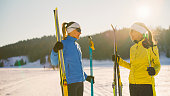 Two women friends holding ski equipment and talking on snowy slope