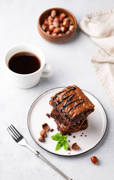 istock A stack of chocolate brownies with mint, hazelnuts and salted caramel on a white plate on a light background with cup of coffee and bowl with nuts. 1748164895