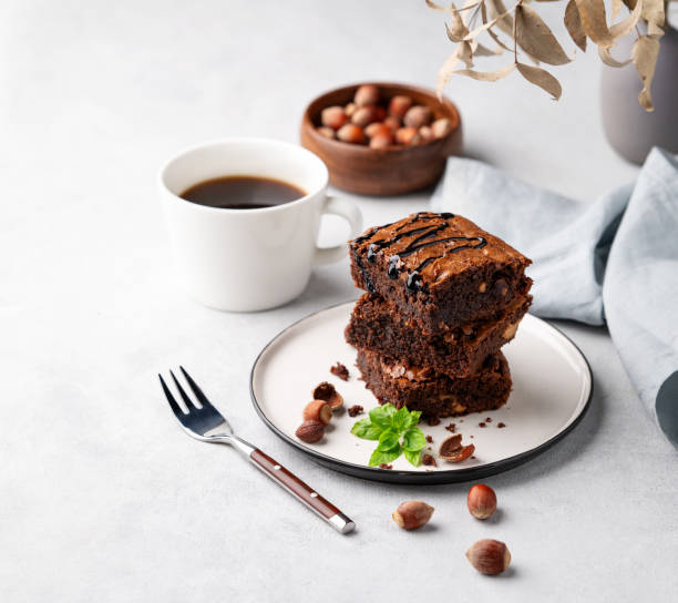 istock A stack of chocolate brownies with mint, hazelnuts and salted caramel on a white plate on a light background with cup of coffee and bowl with nuts. 1748165409