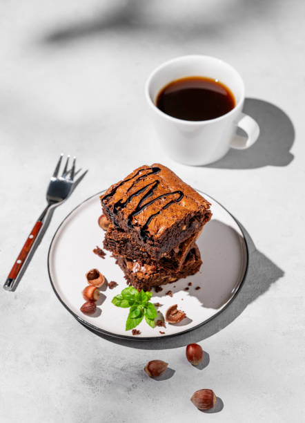 istock A stack of chocolate brownies with mint, hazelnuts and salted caramel on a white plate on a light background with cup of coffee and morning shadows. 1748165415