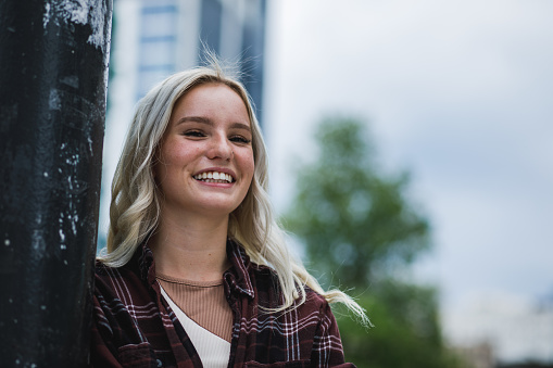 Portrait of charming young blond woman standing on the city street and joyfully smiling at camera.