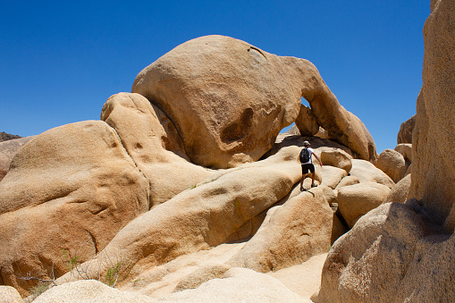 Man climbs through the rocks and boulders on Arch Rock Trail in Joshua Tree National Park, California, USA. Travel concept.