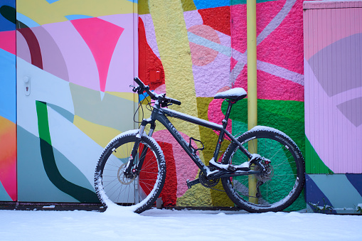 Stuttgart, Germany - December 16, 2022: Mountain bike in front of colorful wall with doors. Two-wheeler in snow. Side view, depth perspective.