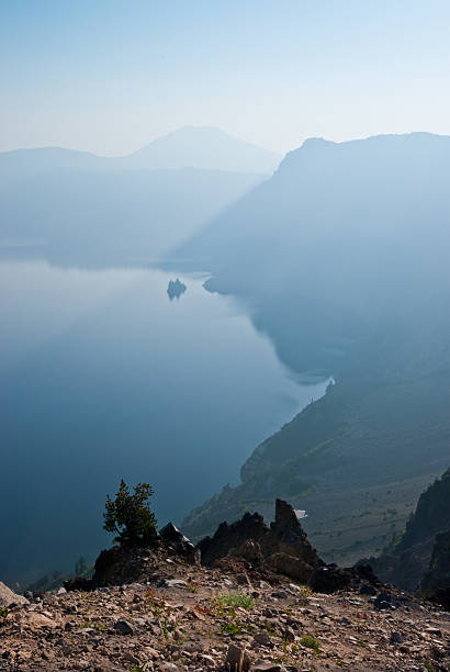 Early Morning Fog Over Crater Lake A combination of early morning fog and smoke from forest fires gives this scene a strange bluish glow. This photograph was captured from Garfield Peak in Crater Lake National Park, Oregon, USA. Phantom Ship and Mount Scott are in the distance. jeff goulden crater lake national park stock pictures, royalty-free photos & images
