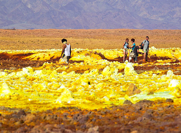 Tourists at Dallol "Tourists walking at fragile Dallol crust as part of Volcanic remains after 1926 eruption of Dallol volcano. It is like Hot Springs with geothermal and volcanic activity with characteristic white, yellow and red colours from sulphur and potassium salts coloured by various ions. It is located in the Danakil Depression with the highest average temperatures on the planet and is considered the most remote and beautiful place on Earth, North East Ethiopia near Eritrea in Africa." dallol ethiopia stock pictures, royalty-free photos & images