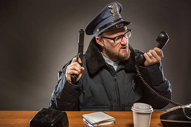 jefe de policía hablando por teléfono con la pistola en la mano - desk police police station humor fotografías e imágenes de stock