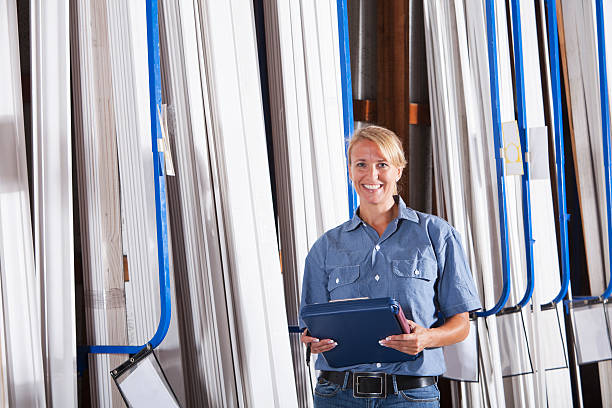 Female worker in building supply store taking inventory Female worker (40s) in hardware store taking inventory of lumber. (Strips of moulding). lumber industry timber lumberyard industry stock pictures, royalty-free photos & images