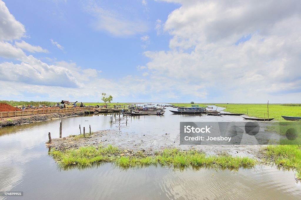 Ganvie Abomey Calavi Dock This is the main departure point to get out to the stilt village of Ganvie in Lake Nokoue in Benin. The skiffs are the primary transportation for the villagers who live in the middle of the lake and fish for a living using the lake as one big fish farm. The people are distant enough to be unrecognizable. Benin Stock Photo