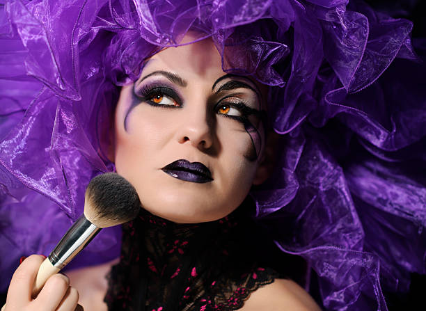 fashion makeup young woman portrait applying makeup, looking up, holding makeup brush. Halloween drag queen stock pictures, royalty-free photos & images