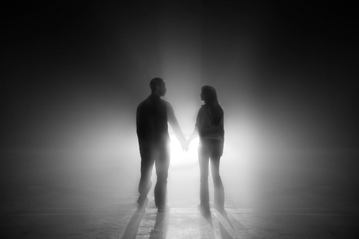 Man and woman are holding hands and walking into light.