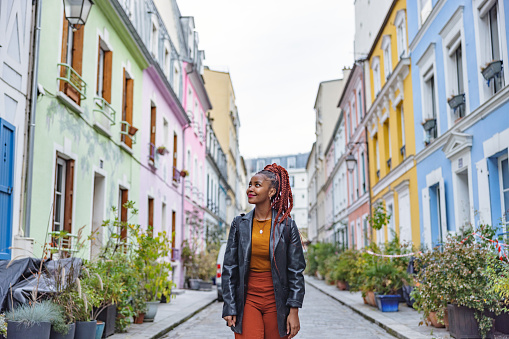 Three-quarter front shot of a casually dressed good looking and young dark-skinned woman walking and sightseeing a multicolored neighborhood located in Paris.