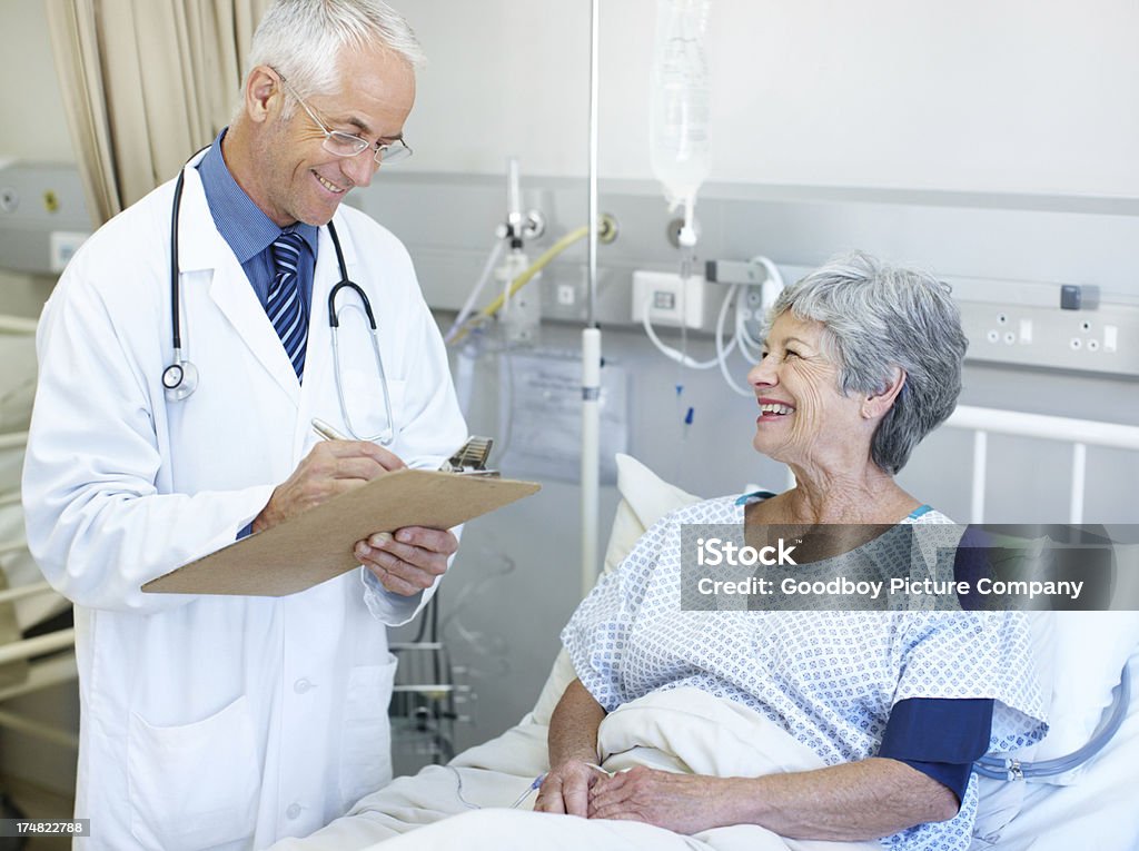 Your results are looking pretty good A doctor reviewing information on a clipboard while talking with one of his patients in a hospital ward Bed - Furniture Stock Photo