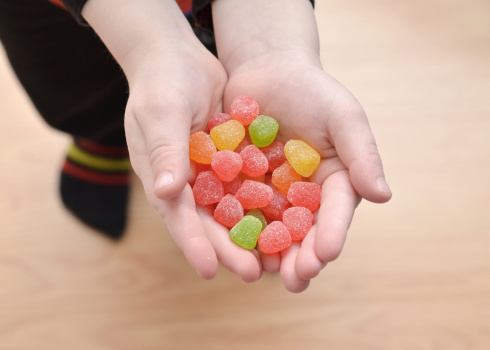 Close up of a young boy holding candy gum drops in his hands.