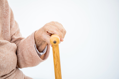 hand of aged woman with cane on light background