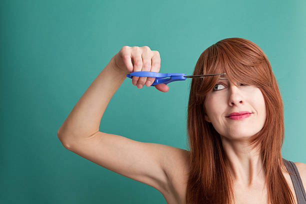 Woman Cutting Her Own Hair A woman with long red hair cutting her bangs with scissors. fringe cut stock pictures, royalty-free photos & images