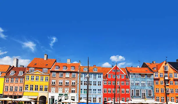 "Colourful townhouses in Nyhavn. Nyhavn is a 17th-century waterfront, canal and entertainment district in Copenhagen, Denmark. It is lined by brightly-coloured townhouses, bars, cafes and restaurants. A major tourist attraction, the canal has many historical wooden ships."