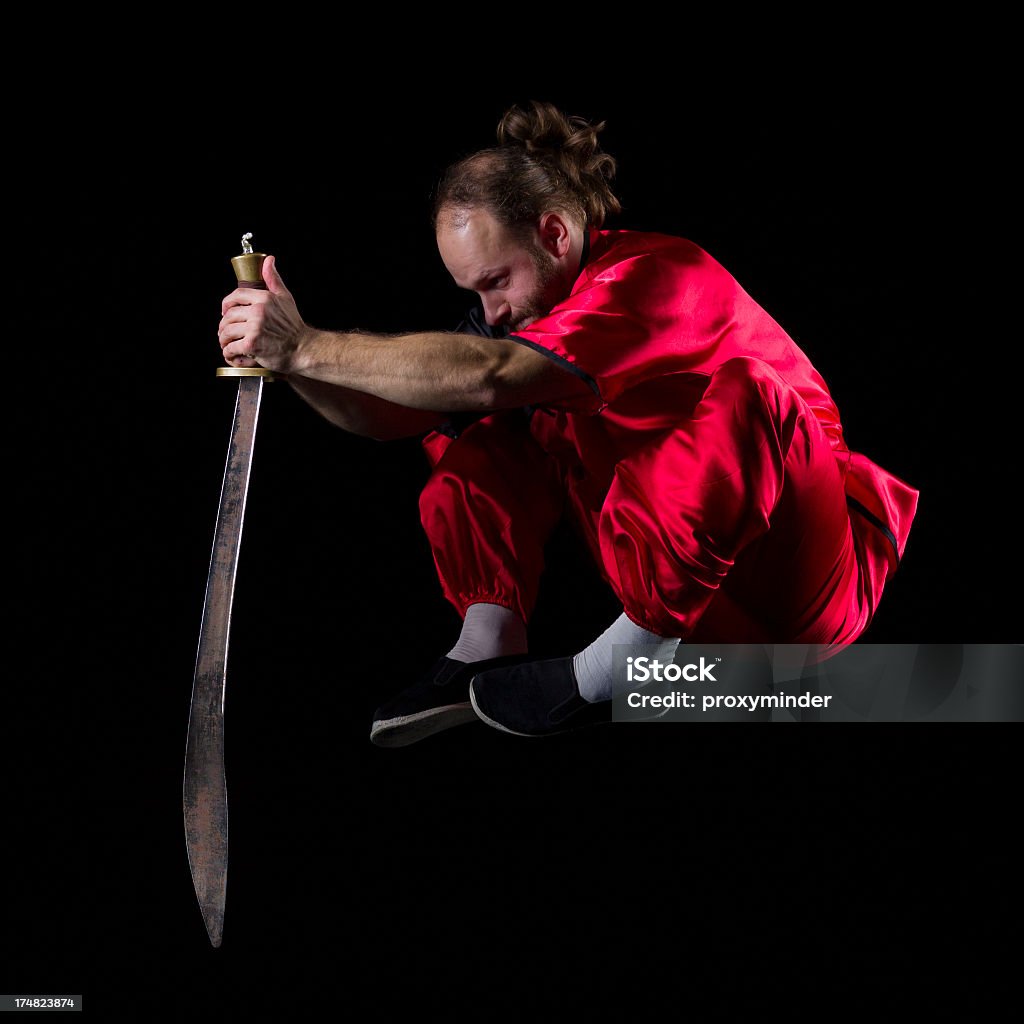 Shaolin Kung Fu fighting position with Dao sword in midair Martial artist isolated on black  Activity Stock Photo