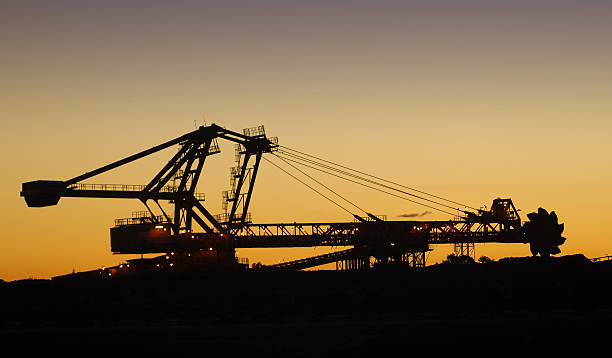 Reclaimer silhouette and iron ore stockpile A silhouette of a reclaimer used to move stockpiles of crushed ore on a mine site. Reclaimer stock pictures, royalty-free photos & images