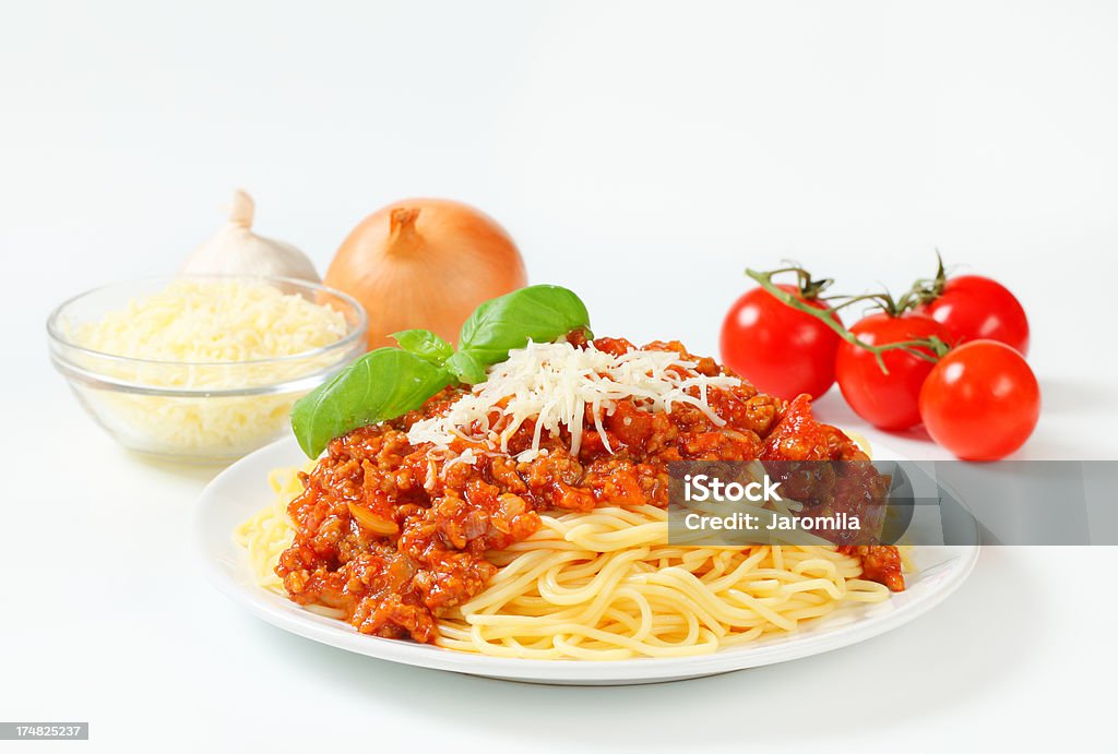 spaghetti bolognese with cheese and vegetables "plate of spaghetti bolognese decorated with grated parmesan cheese and basil leaves, bowl of grated parmesan cheese and vegetables" Bolognese Sauce Stock Photo