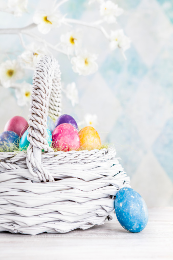 Colourful Easter eggs sitting in a white basket.Colorful Easter Eggs sitting in a bowl with Easter decorations hanging in the background.