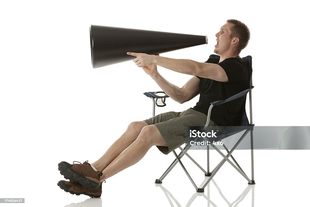 Hombre sentado en una silla plegable y gritar en bullhorn - Foto de stock de 20 a 29 años libre de derechos