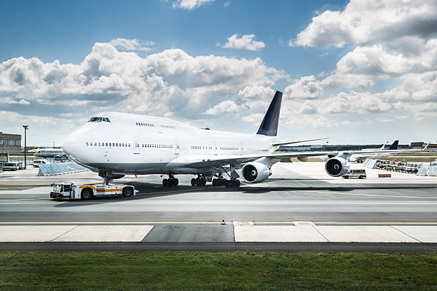 A jumbo jet gets parked nearby a runway with white clouds