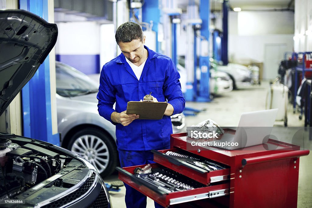 Everything checks out A mechanic looking over a checklist while doing an engine service Laptop Stock Photo